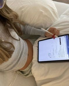 a woman laying in bed while holding an electronic device with a pen and eyeglasses on it