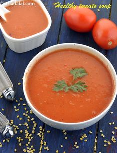 two bowls of tomato soup on a blue table with tomatoes and parsley in the background