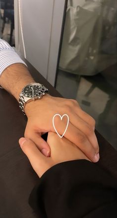 a person holding the hand of another person with a watch on their wrist and wearing a heart - shaped ring