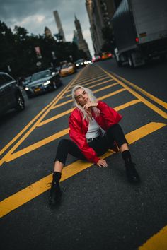 a woman sitting in the middle of an empty street with her hand on her chin