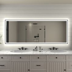 a bathroom vanity with two sinks and a large mirror above it that lights up the room