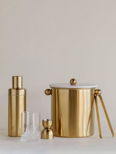 a gold ice bucket with two glasses next to it on a white surface, and the lid is open