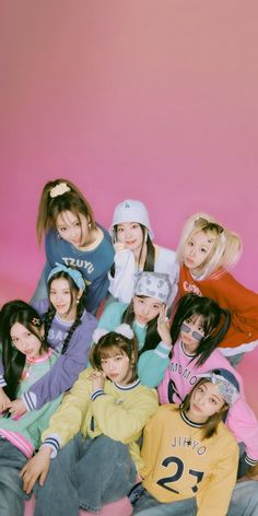 a group of young women sitting next to each other in front of a pink wall