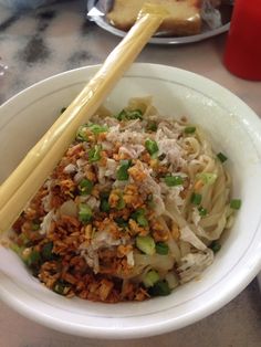 a white bowl filled with noodles and meat next to chopsticks on a table