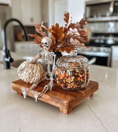 a skeleton is sitting on a table next to a glass jar filled with nuts and leaves