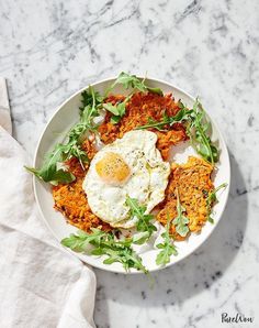 a white bowl filled with fried eggs and greens on top of a marble countertop