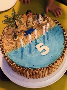 a birthday cake that is decorated with figures and sand on the beach for a five year old