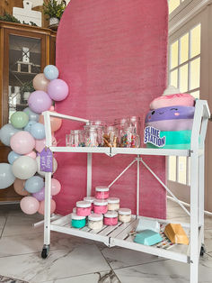 a shelf with cake, candles and balloons in front of a large pink wall behind it