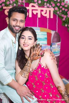 a man and woman pose for a photo in front of a backdrop with pink flowers