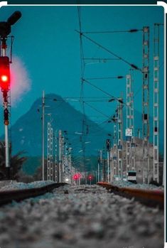 a red traffic light sitting on the side of a train track next to a mountain