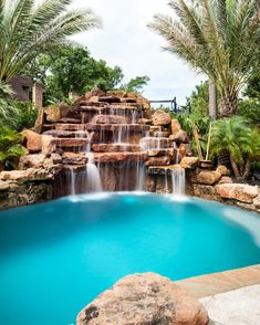 a pool with waterfall and palm trees in the backround, surrounded by rocks