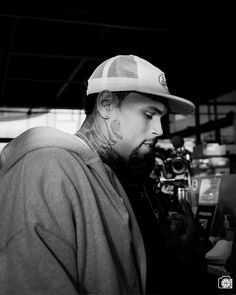 a man with tattoos on his face wearing a baseball cap and looking down at the camera