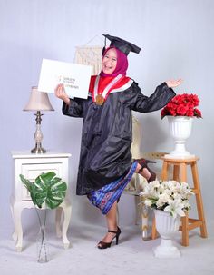 a woman wearing a graduation gown and holding a sign in front of a table with flowers