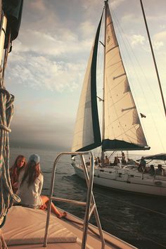 two women sitting on the deck of a sailboat in the ocean at sunset or sunrise