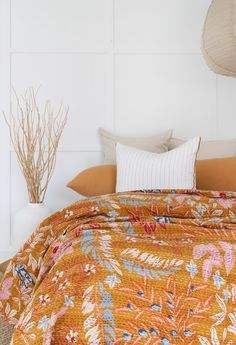 a bed with an orange floral comforter and pillows on it, next to a wicker basket