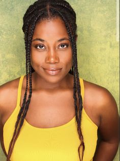 a woman with braids standing in front of a green wall wearing a yellow tank top