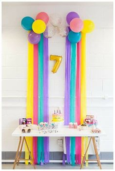 a table topped with balloons and streamers next to a number one balloon wall hanging from the ceiling