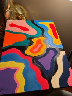 an abstract painting is displayed on a table with a gold lamp in the back ground