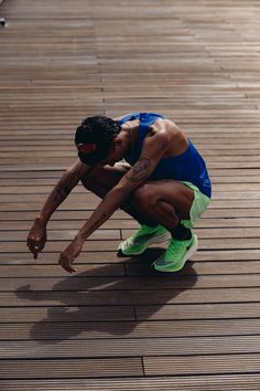 a man crouching down on a wooden floor with his hands in his pockets and headphones to his ear