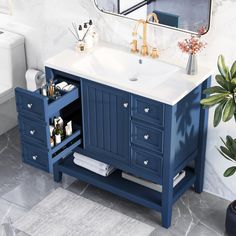 a bathroom vanity with blue drawers and white counter top, gold faucet mirror above it