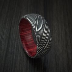 a silver ring with red wood in the middle on a wooden surface, close up