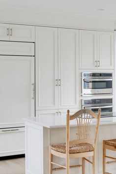 a kitchen with white cabinets and two chairs in front of an island counter top oven