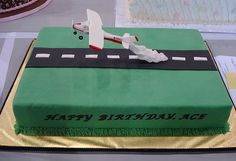 a green birthday cake with an airplane on the road and happy birthday written on it