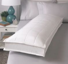 a white bed with pillows on top of it and a night stand in the background