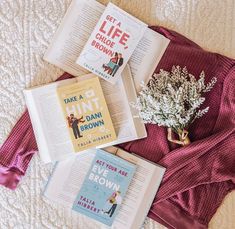 three books laying on top of a bed next to a bouquet of flowers and an open book