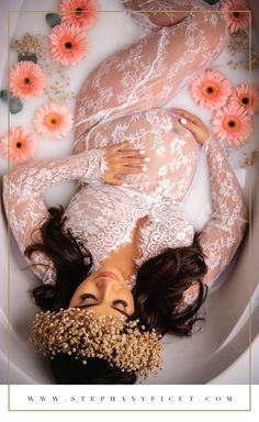 a pregnant woman laying in a bathtub with flowers around her head and body on the side