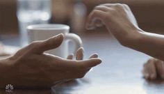 two hands reaching out towards each other over a table with coffee mugs on it