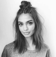 a young woman with long hair wearing a sweater and looking at the camera while standing in front of a white wall