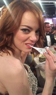 a woman holding a toothbrush in her mouth at a dinner table with other people