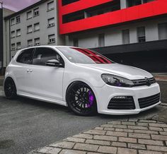 a white car parked in front of a red and grey building with black rims