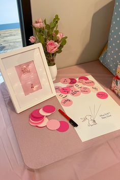 a table topped with pink and white cards next to a vase filled with flowers on top of a bed