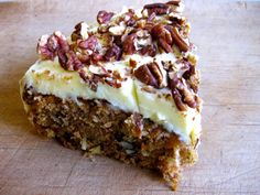 a piece of carrot cake with white frosting and pecans on top is sitting on a cutting board