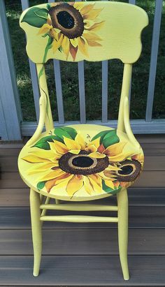 a yellow painted chair with sunflowers on the back and sides, sitting on a deck