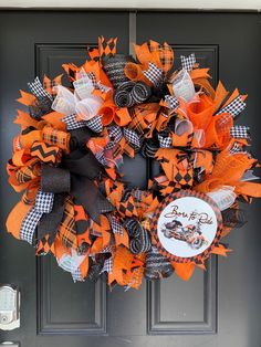 an orange and black wreath on the front door is decorated with pumpkins, checkered ribbon and ribbons