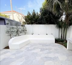 a white bench sitting next to a tree in a backyard with stone tiles on the ground