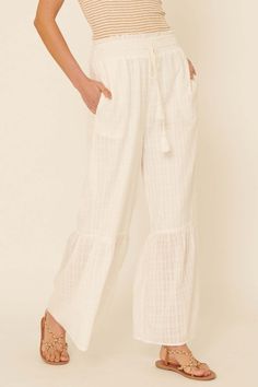 Tonal plaid cotton pants. Smocked elastic waist with raw-edge ruffle. Drawstring with tassel ties. Wide leg. Flared ruffle hem. Side pockets. Partial lining. Loose fit. 100% Cotton. Imported. Designed in LA. Model wears size S. Cotton Ruffle Long Pants, White Cotton Bottoms With Ruffle Hem, Beach Wide Leg Bottoms With Ruffles, Cotton Ruffled Bottoms For Beach, Casual Ruffled Pants For Vacation, Wide Leg Ruffled Bottoms For Loungewear, Casual Ruffled Relaxed Fit Pants, Casual White Bottoms With Ruffle Hem, Cotton Pants With Tie Waist