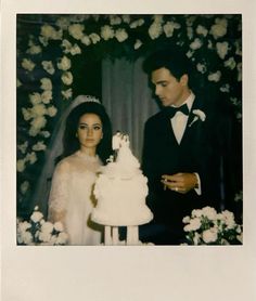 a man and woman standing next to each other in front of a white wedding cake