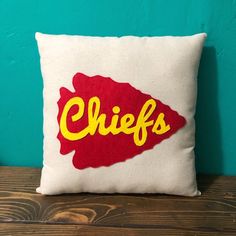 a pillow with the word chiefs on it sitting on top of a wooden table next to a blue wall