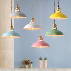 four multicolored lamps hanging from a ceiling in a room with blue walls and planters