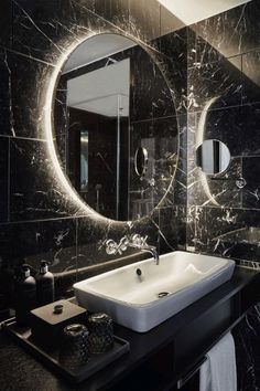 a bathroom with black marble walls and white sink in front of a large round mirror