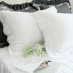 a white bed topped with lots of pillows next to a book and flower vase on top of it