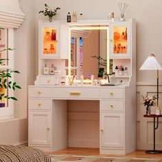 a white vanity with lighted mirror and drawers in a room next to a lamp on the floor