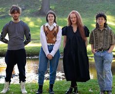 four people standing next to each other in front of a body of water and trees