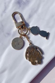 a key chain with two charms attached to it on a marble surface, one has a leaf and the other has a fish