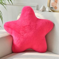 a pink star pillow sitting on top of a white couch next to a potted plant