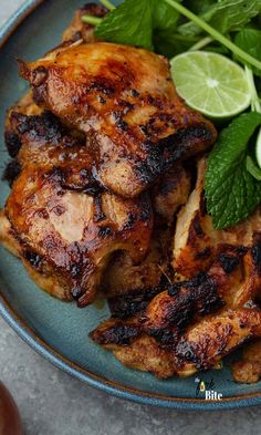 a blue plate topped with grilled chicken next to green leaves and lemon wedges